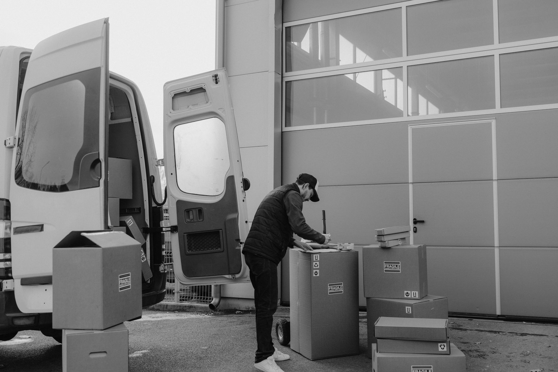 Person loading boxes into a delivery van outside a building with a closed garage door.