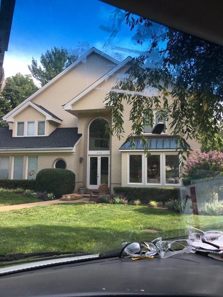 A large house with a lot of windows is seen through the windshield of a car.