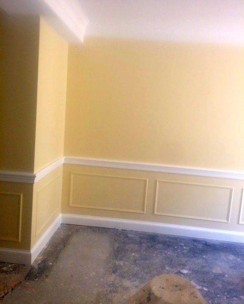 A room with yellow walls and white trim is being painted.