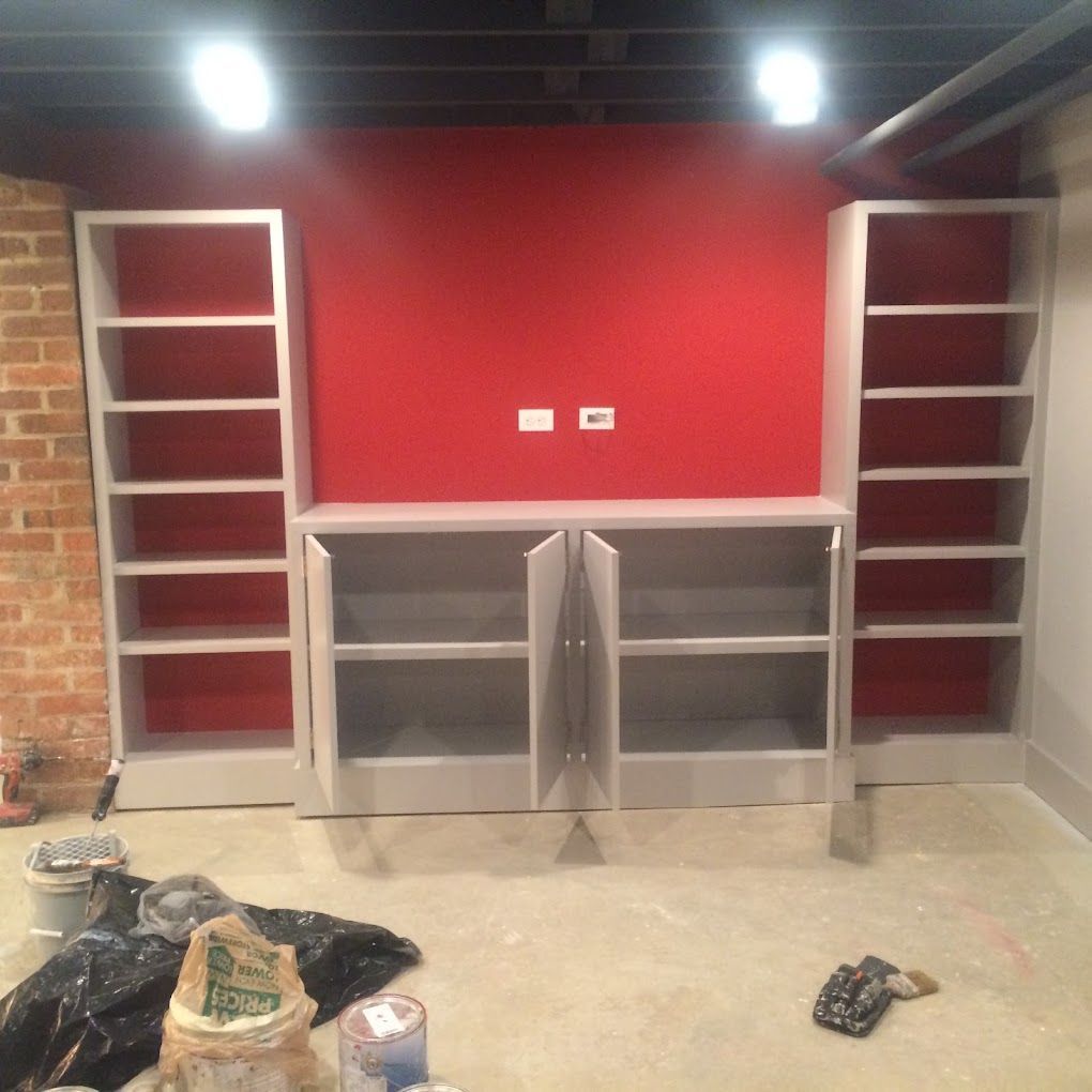 An empty room with a red wall and shelves with a bag of paint on the floor