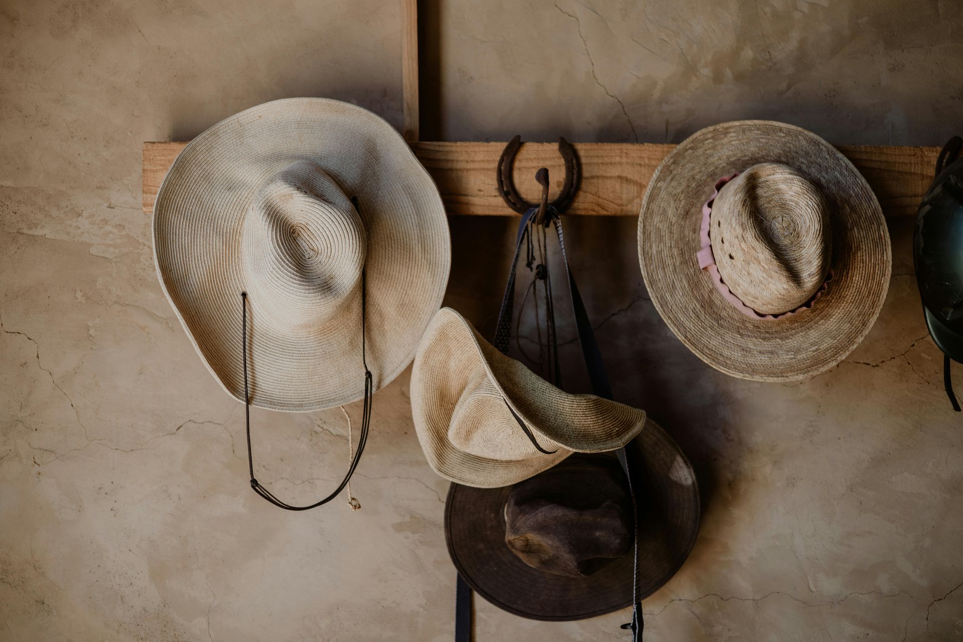 Three cowboy hats are hanging on a wooden rack.