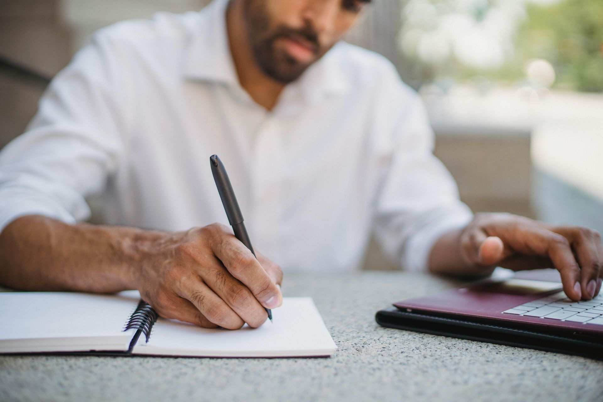 A man is sitting at a table writing in a notebook.