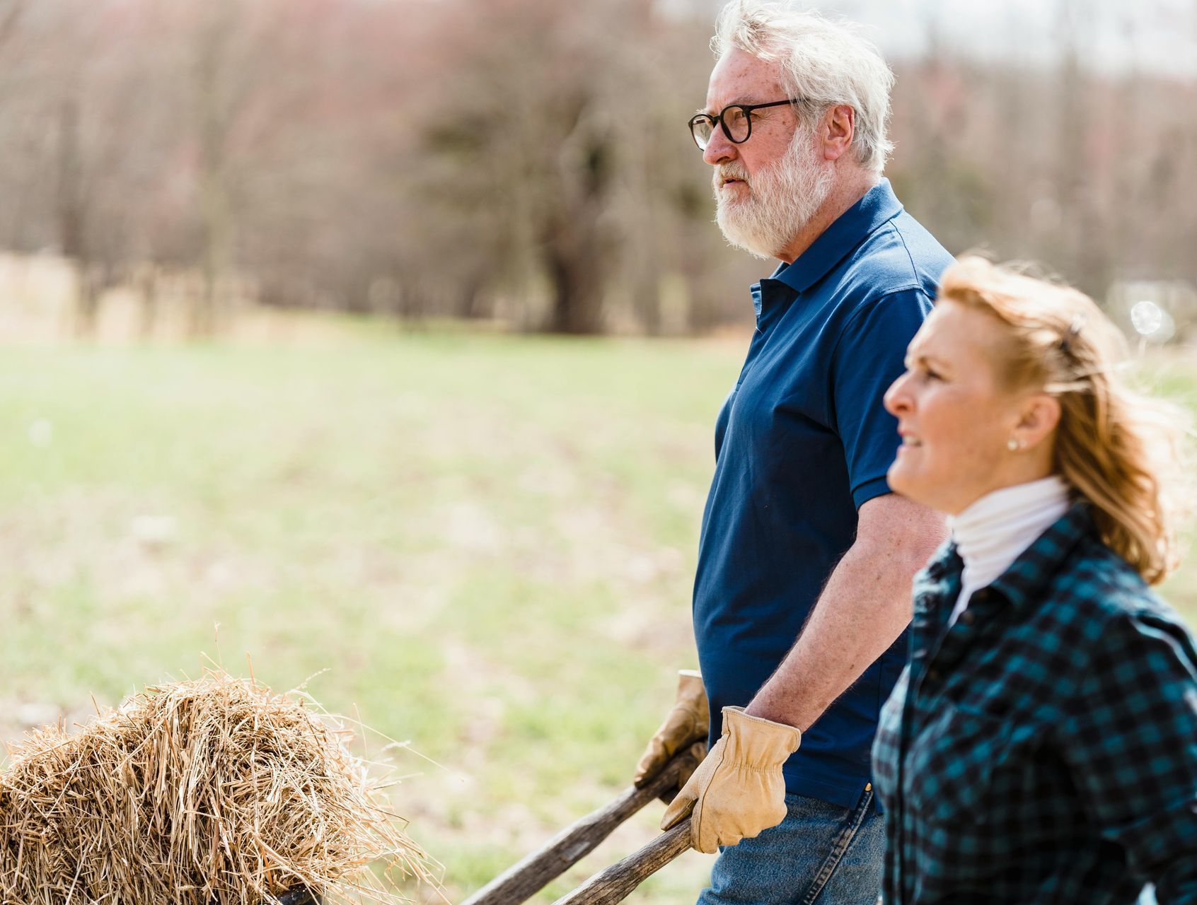 A man and a woman are pushing a cart full of hay.