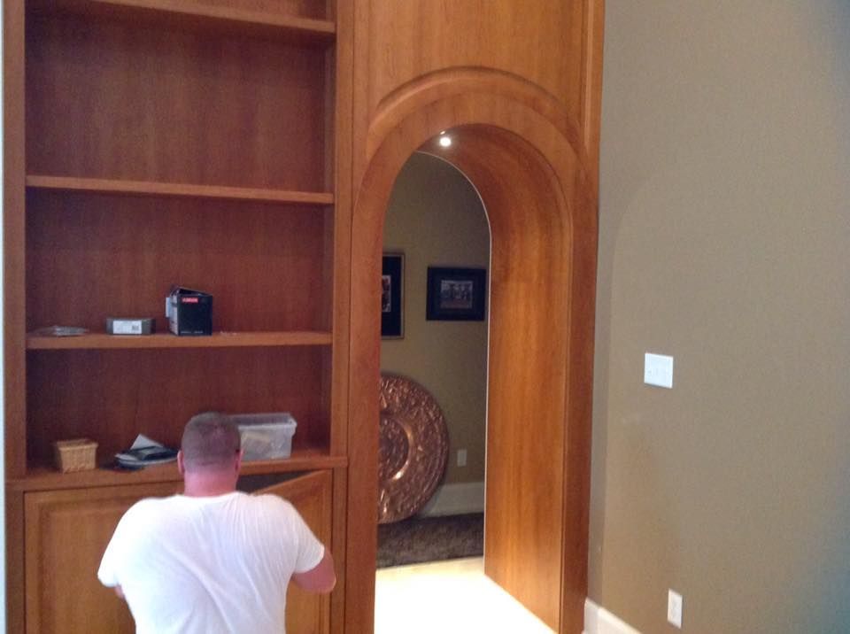 A man in a white shirt is standing in a hallway next to a bookshelf