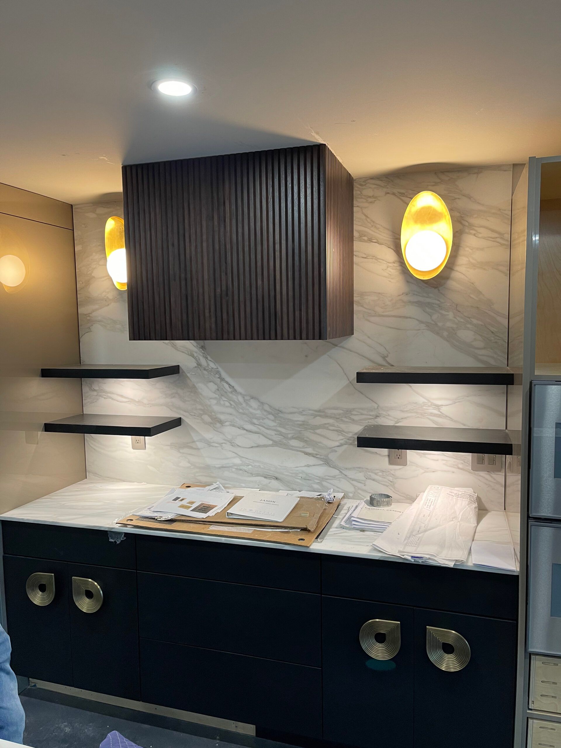 A kitchen with a marble counter top , black cabinets , and a hood.