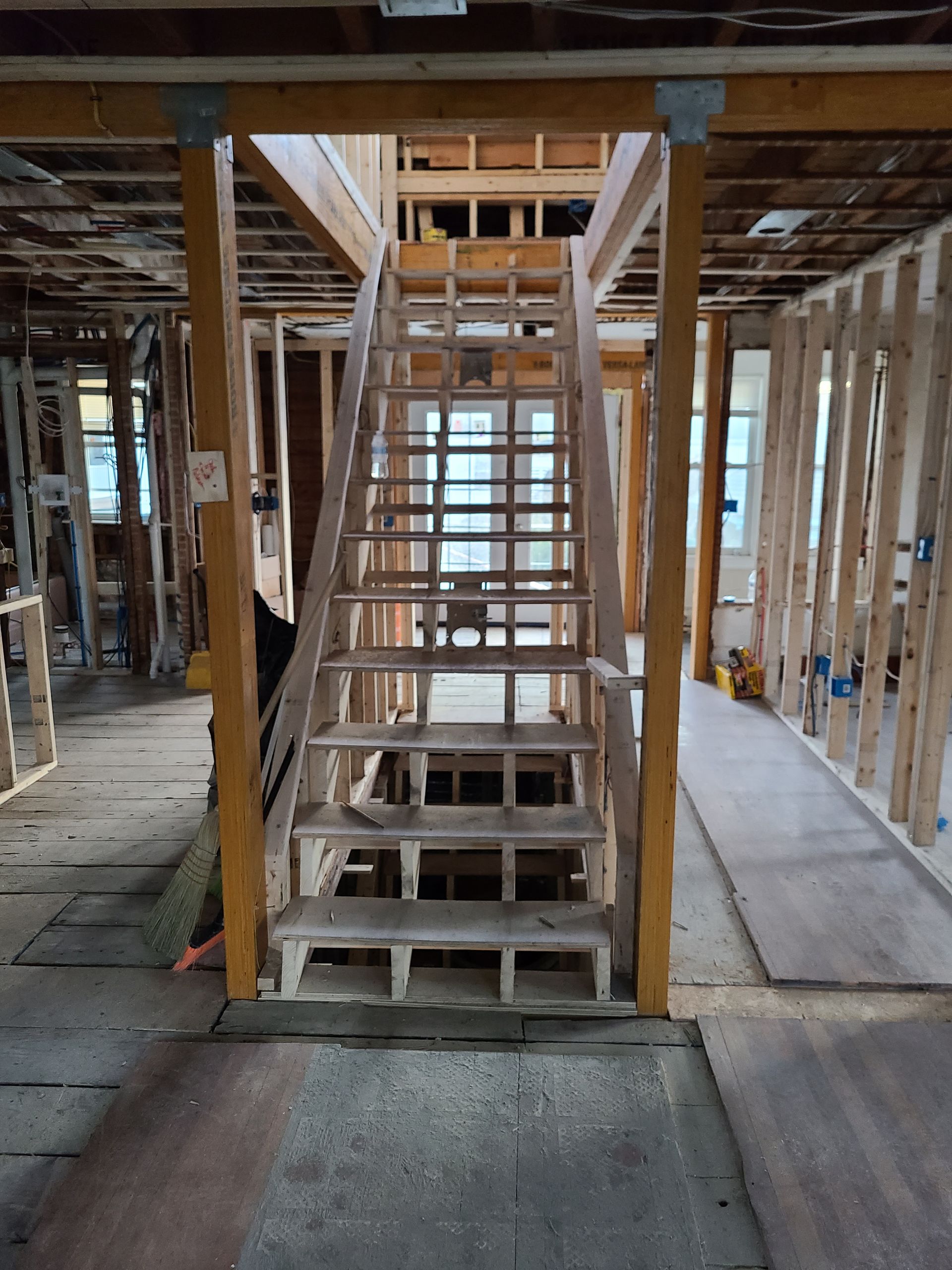 A partially constructed wooden staircase centered in an open-framed building with exposed wall studs and subflooring.