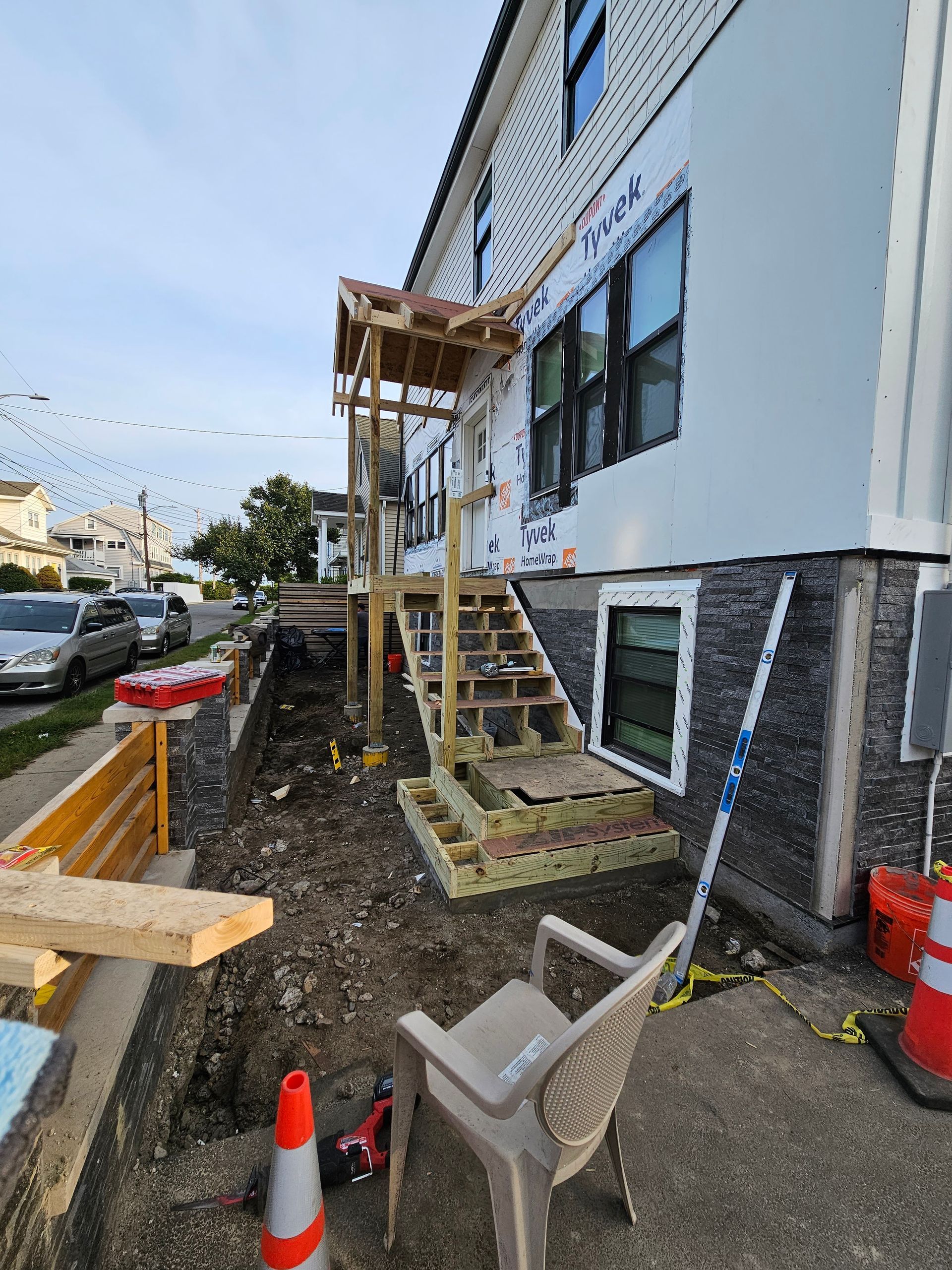 Construction scene of a residential exterior with a partially built wooden staircase and scaffolding.