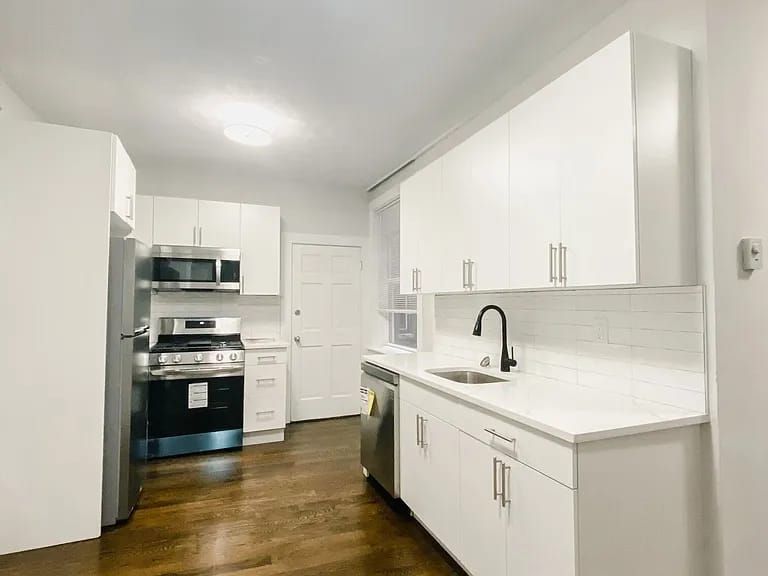 Modern kitchen with white cabinets, stainless steel appliances, a subway tile backsplash, and dark hardwood floors.