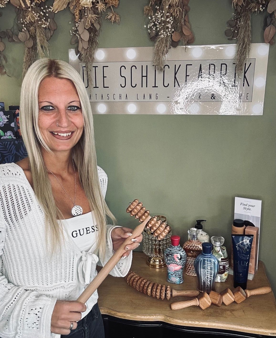 Eine Frau hält einen Holzstab vor einem Schild mit der Aufschrift „Die Schickfabrik“
