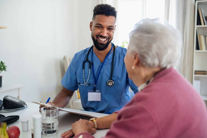 A Nurse Is Talking To An Elderly Woman Who Is Sitting At A Table — Billings, MT — TJ Staffing Inc.