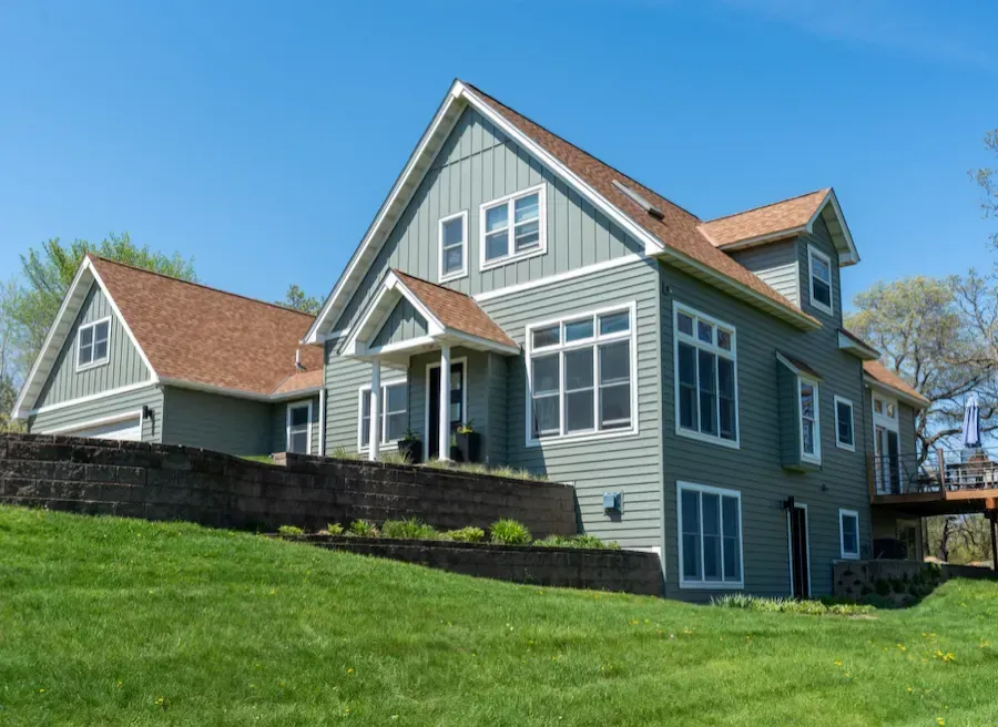 Two-story green house with white trim, brown roof, and a grassy lawn. Blue sky in the background.