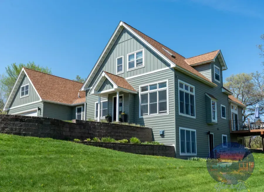 Two-story green house with white trim, brown roof, and a grassy lawn. Blue sky in the background.