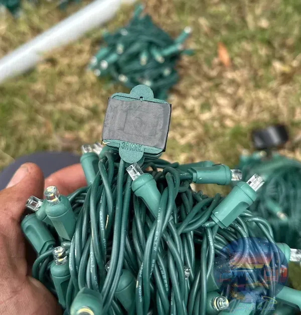 Close-up of a hand holding a tangled bundle of green Christmas lights with a label attached.