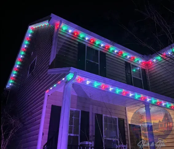 House with red, green, and blue Christmas lights along roof lines and porch. Dark night setting.