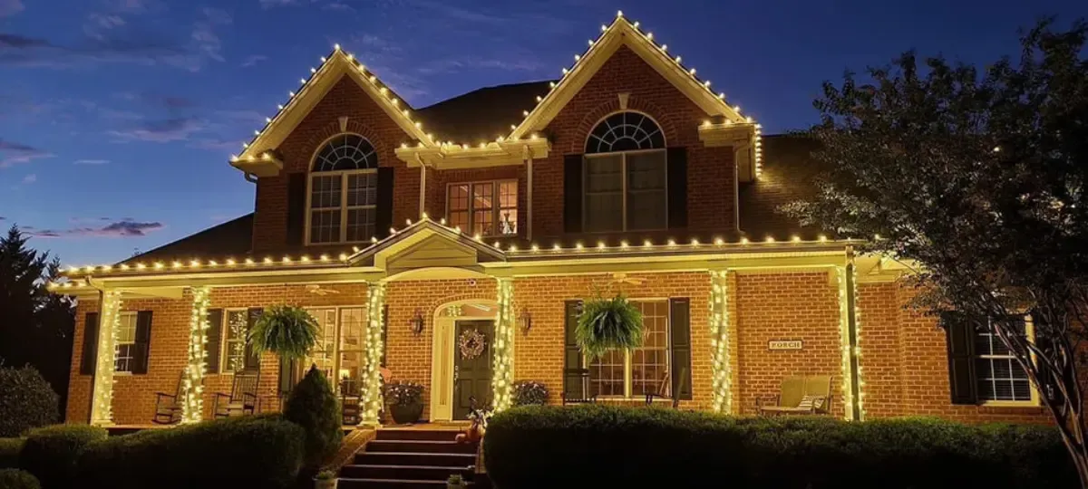 A brick house at dusk, lit with white Christmas lights.
