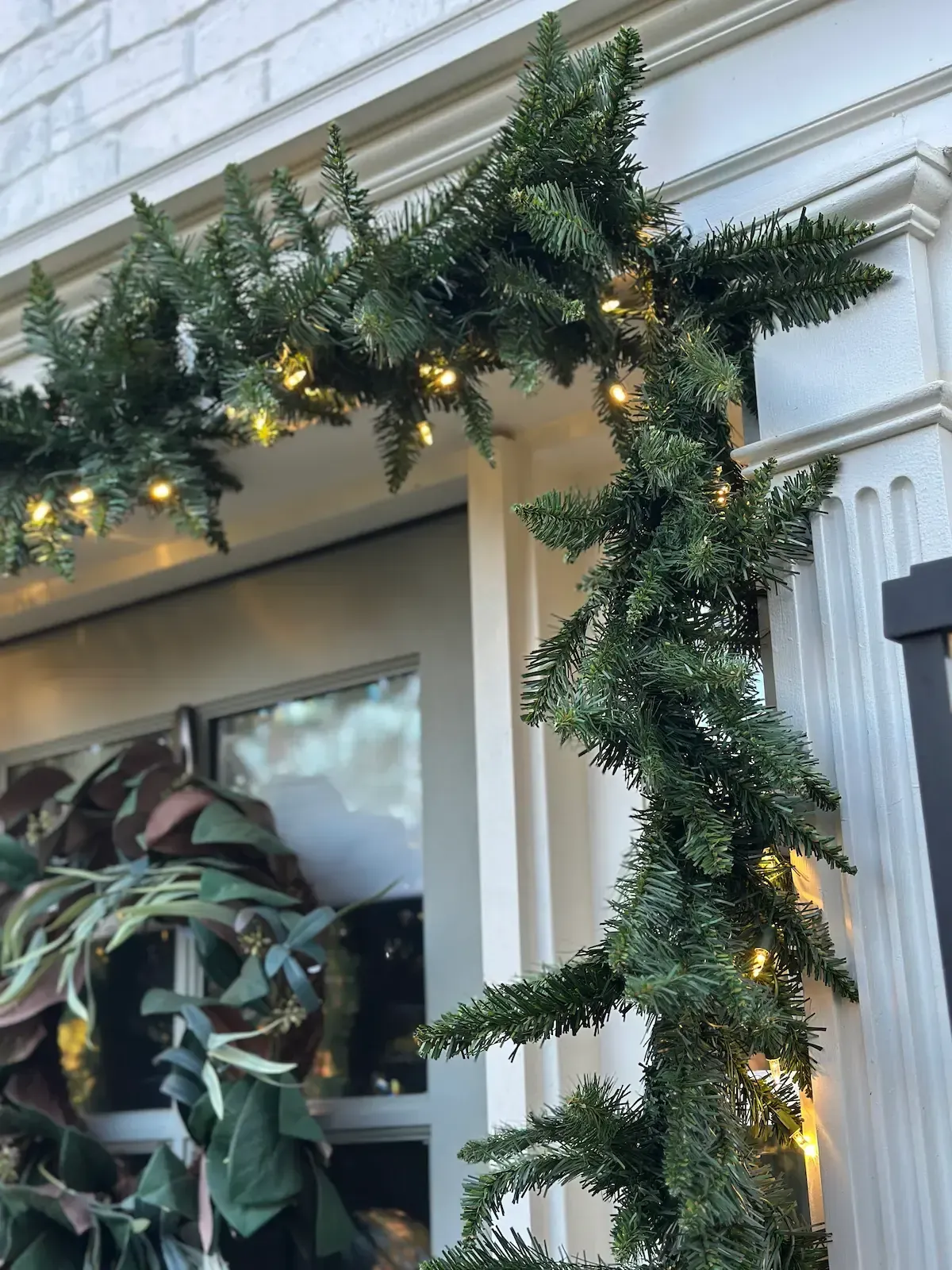 Green garland with fairy lights decorates a white doorway for the holidays.