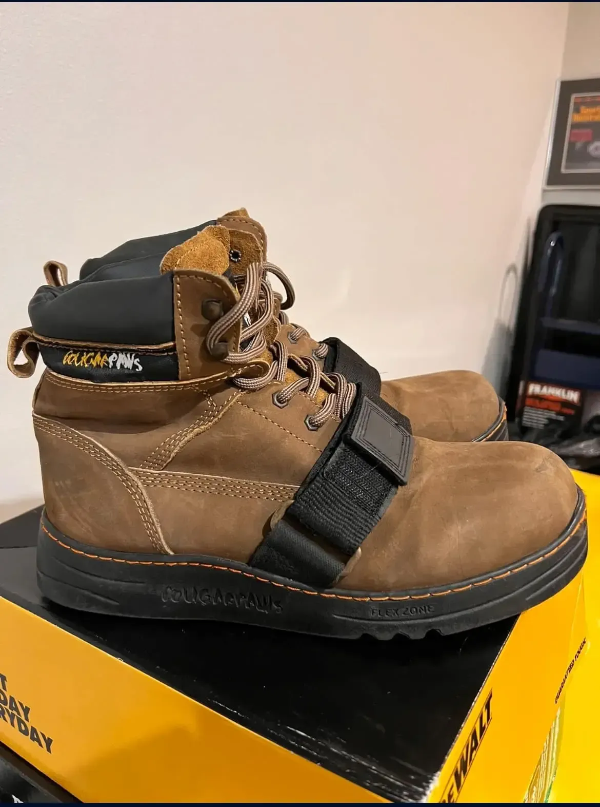 Brown work boot with black strap and sole, sitting on a yellow box.