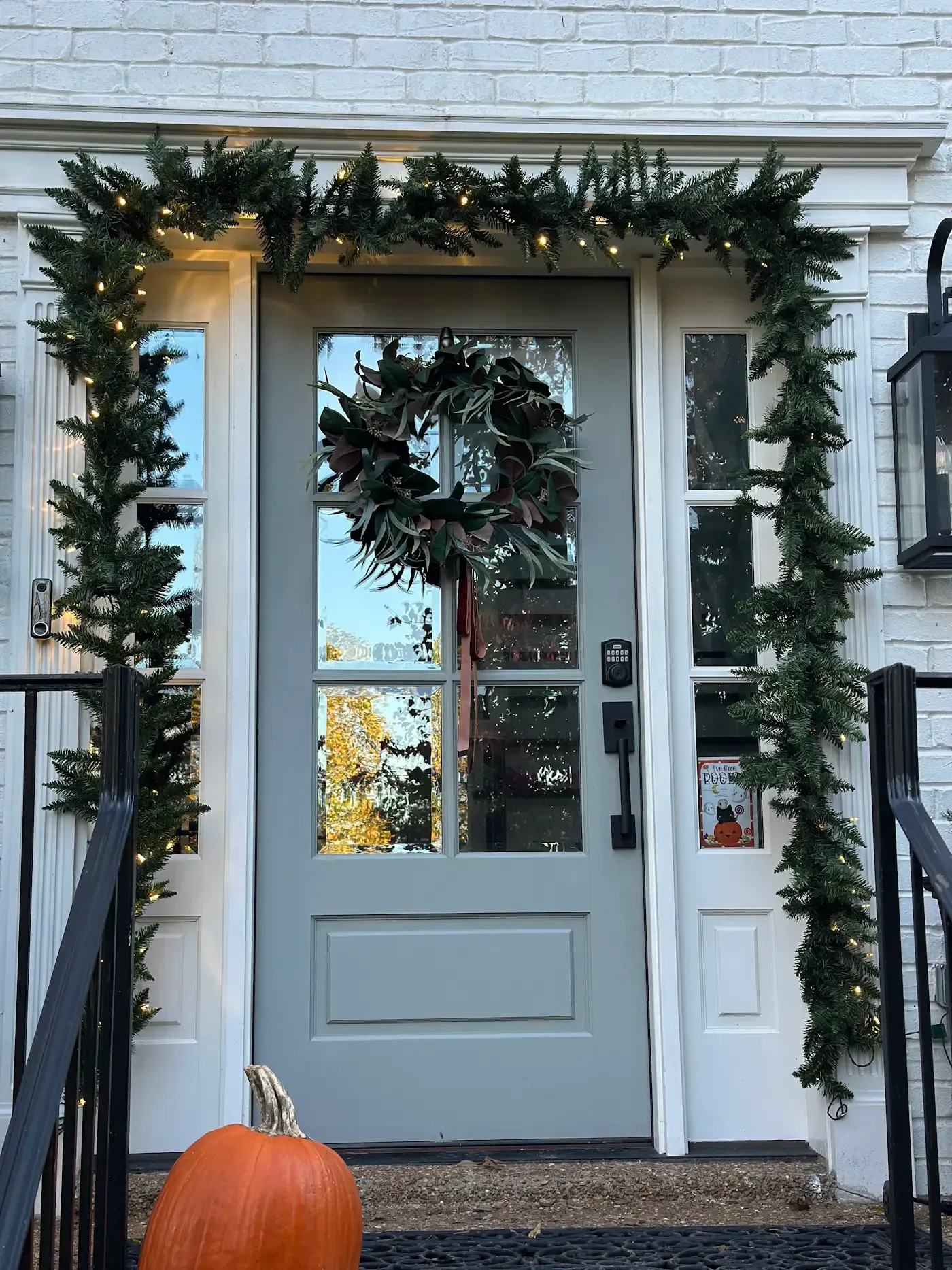 Grey front door decorated with garland, wreath, and pumpkin.