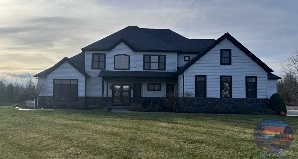 Two-story white house with black roof and trim, front porch with a stone base on a grassy lawn.