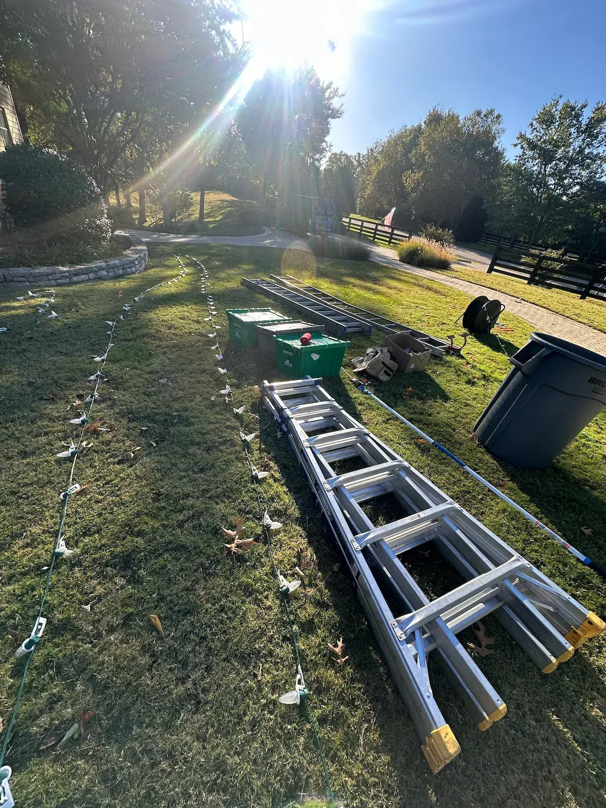 Ladders, tools, and materials scattered on grass under a sunny sky; likely a construction or renovation site.