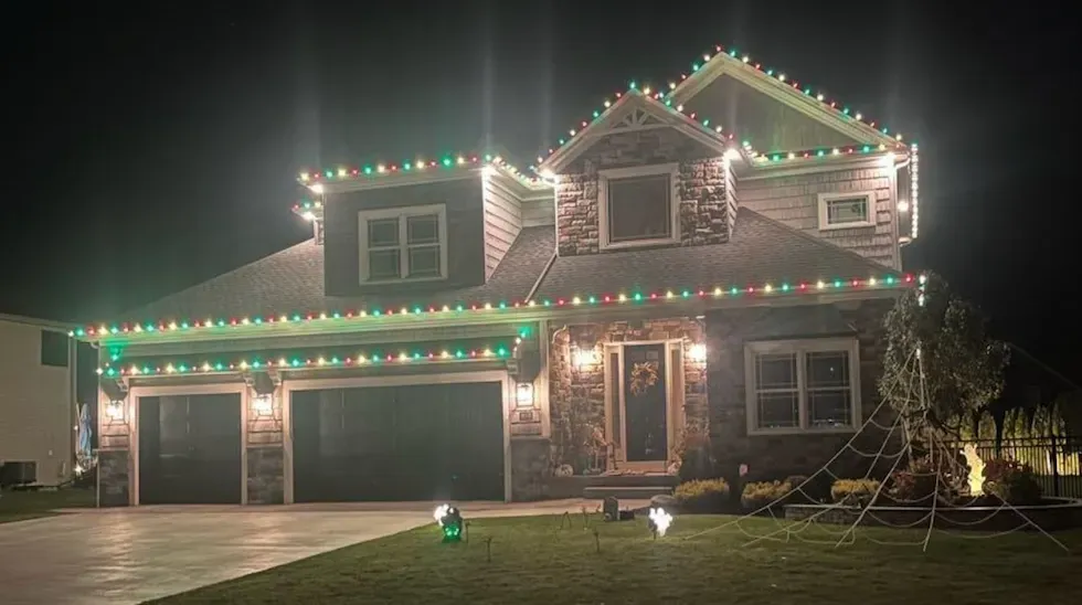 A two-story house at night, decorated with red and green Christmas lights along the roofline.