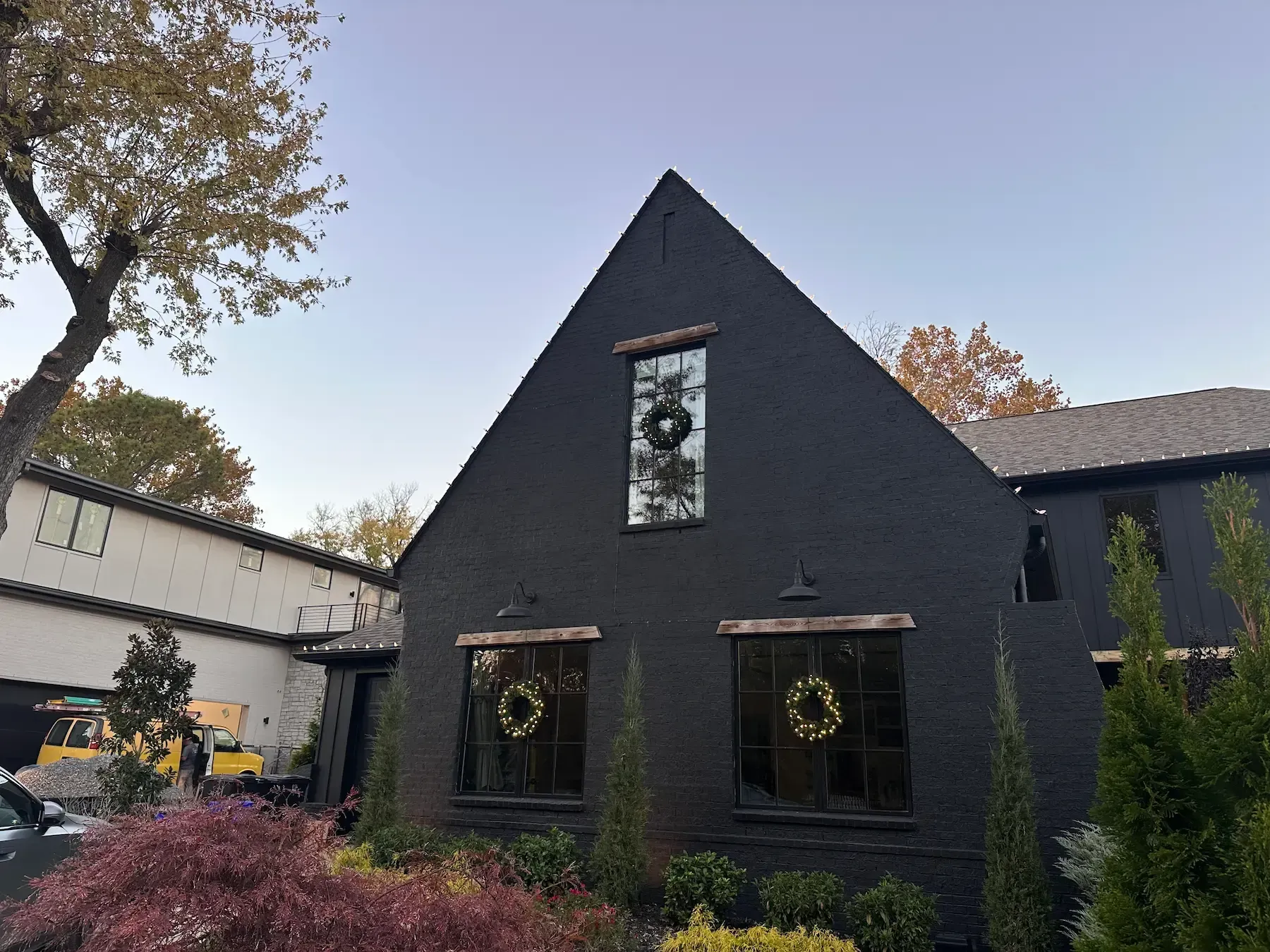 Black house with triangular roof and wreaths in windows; bushes in front.