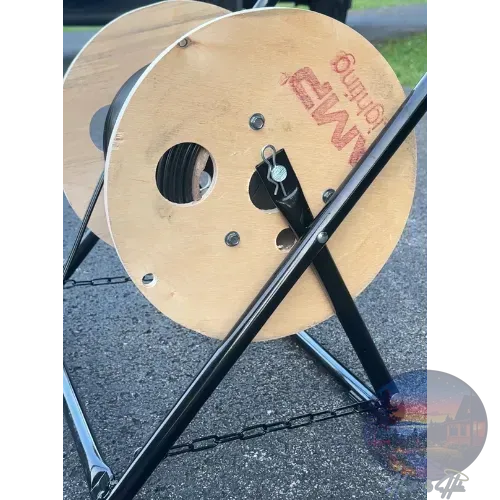 Cable reel with black metal frame, on pavement. Wooden spool has black cable wrapped on it.