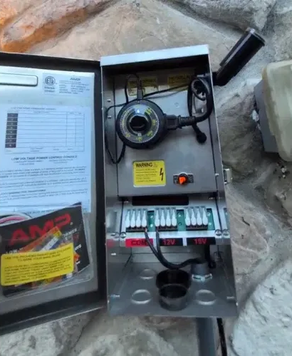 Open outdoor electrical box with timer and wiring for landscape lighting.