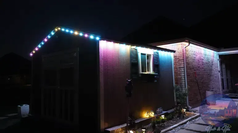 Night shot of a shed and house lit with colorful Christmas lights.