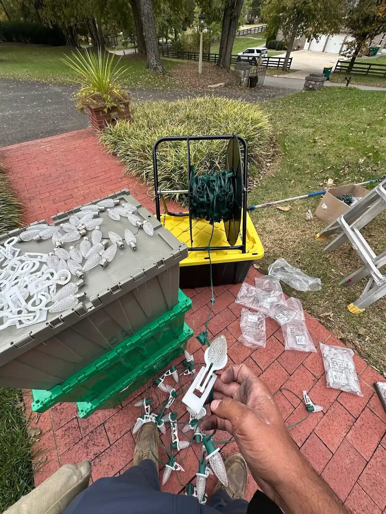 Person installing lights on a house. Green and white lights, brown and green containers, black reel.