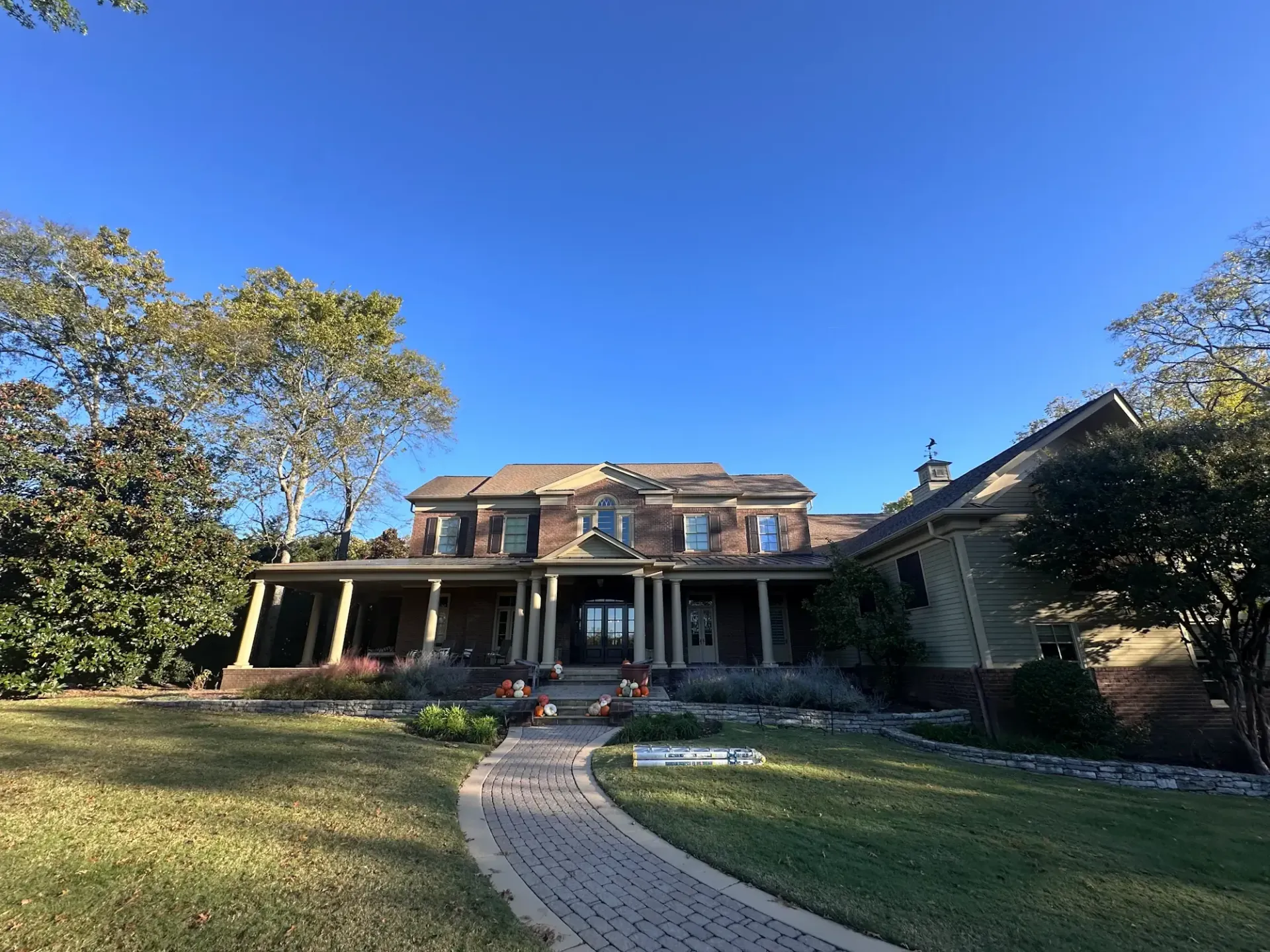 Large two-story house with a brick facade and a long porch. A brick pathway leads up to the front door.
