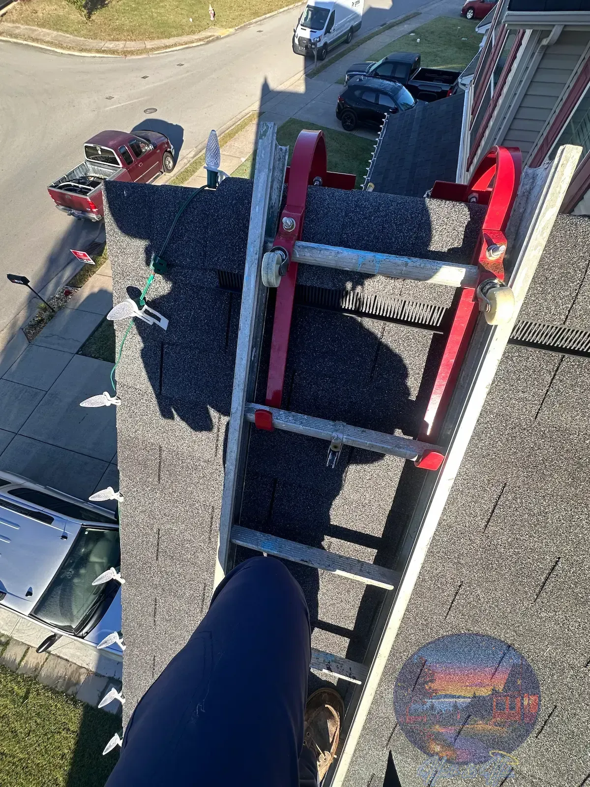 A ladder with two red hooks latched onto the peak of a roof