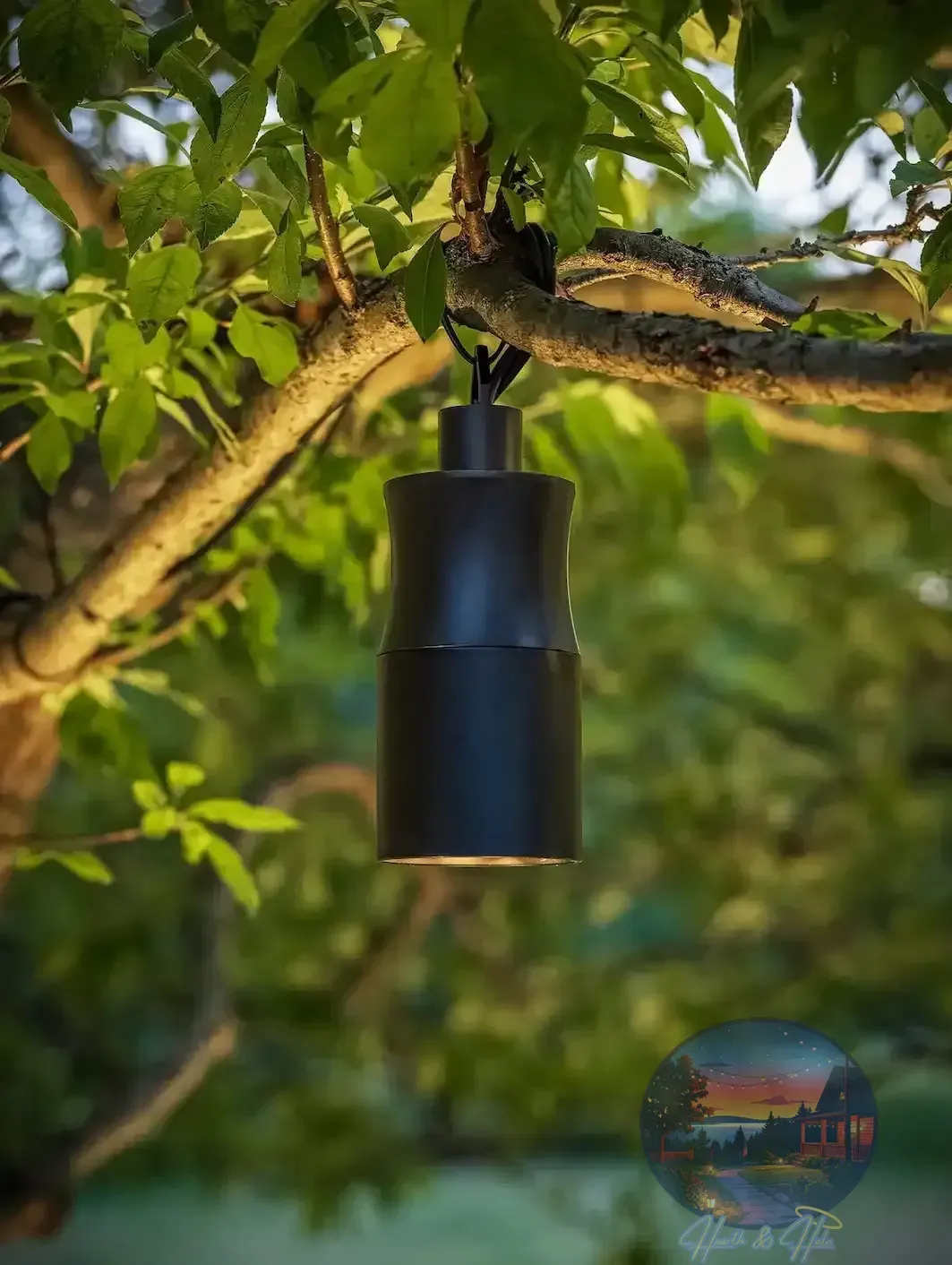 Dark, cylindrical outdoor light fixture hanging from a tree branch, illuminating the surrounding leaves.