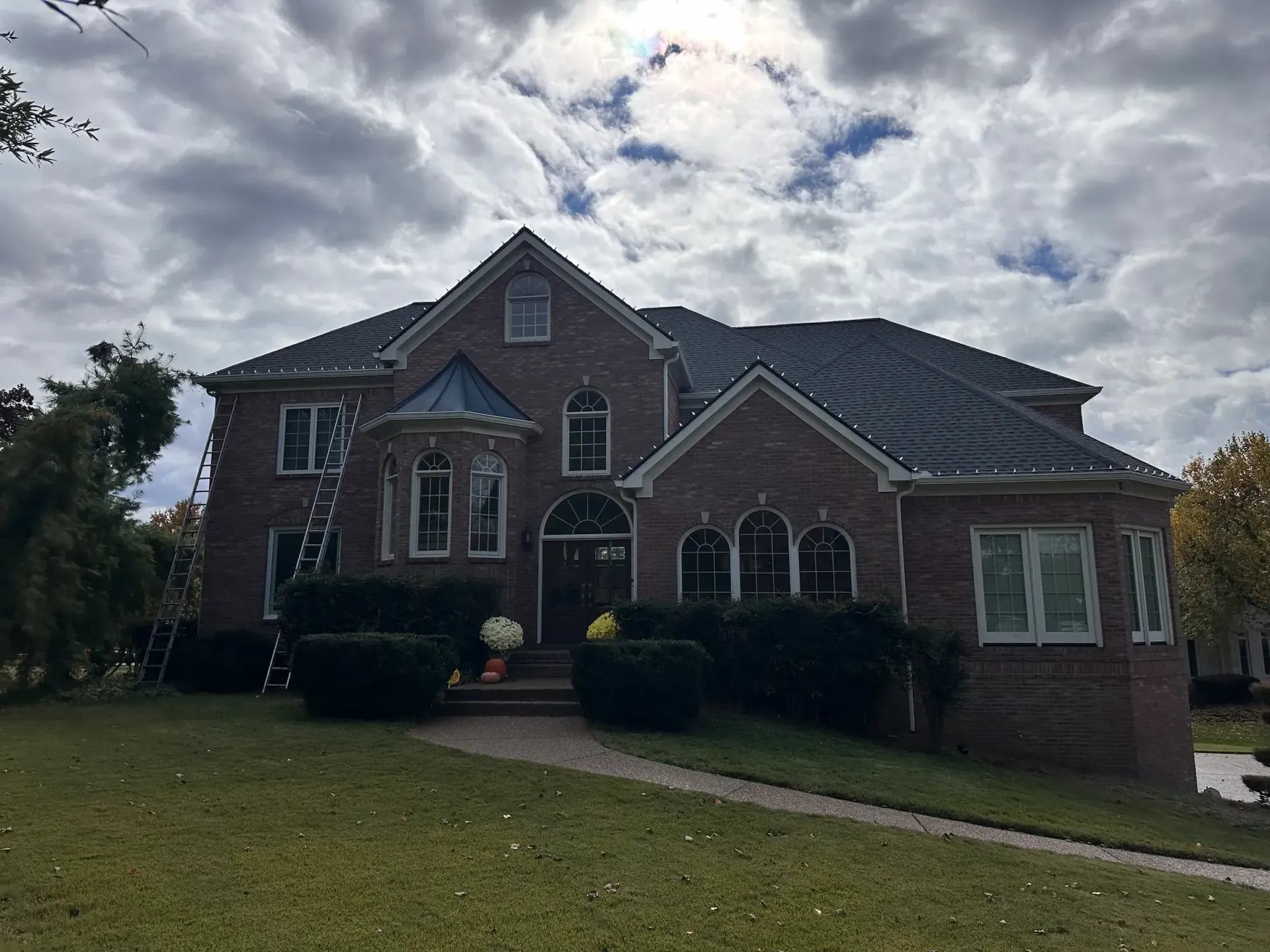 Two-story brick house with dark roof and landscaping under a cloudy sky.