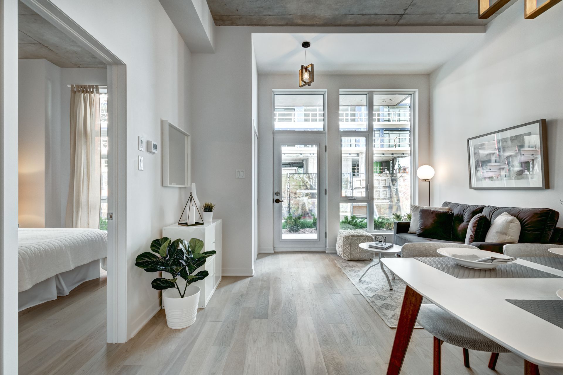 A couple sits on the floor with mugs, laughing amidst cardboard moving boxes in a bright, sparsely furnished room.