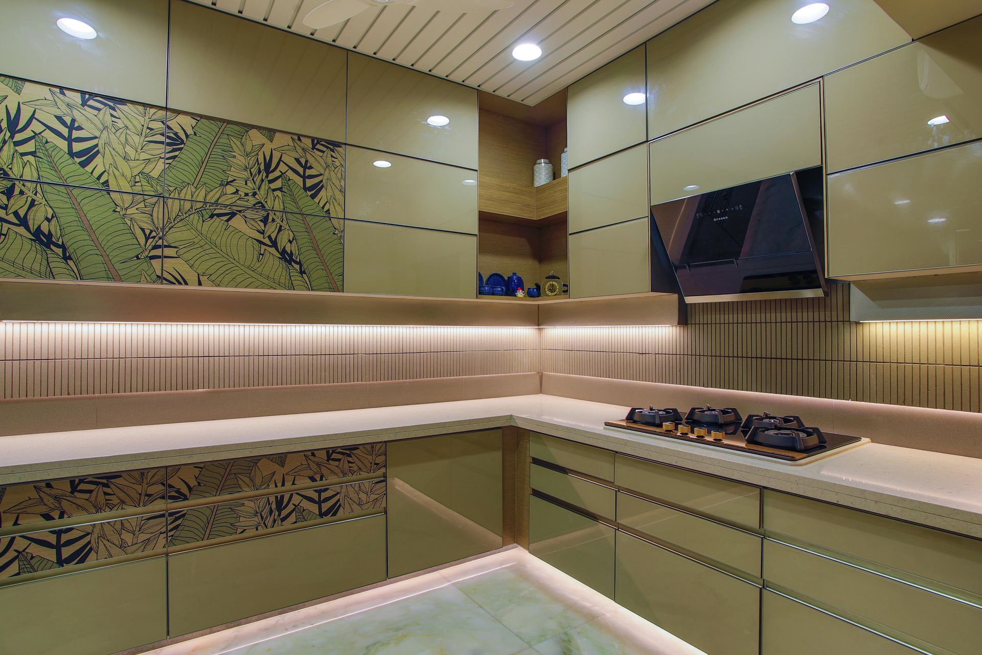 A modern kitchen with sage green cabinets, patterned panels, warm under-cabinet lighting, and a dark glass stove.