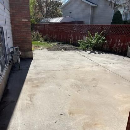 A concrete driveway in front of a house with a red fence.