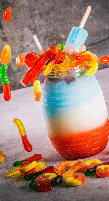 A colorful drink with gummy bears and popsicles in a glass.