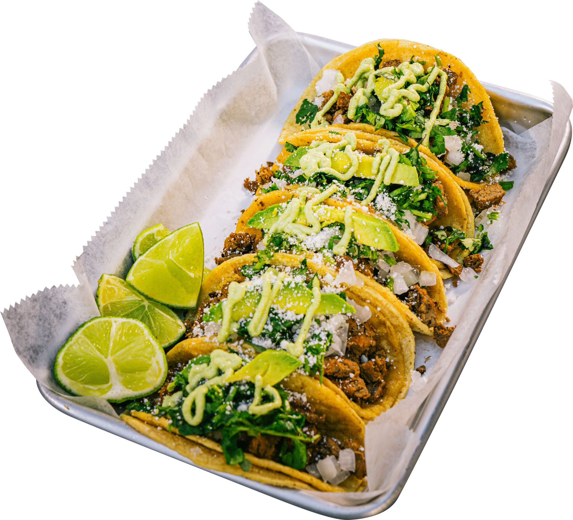 A tray of tacos with limes and avocado on a white background.