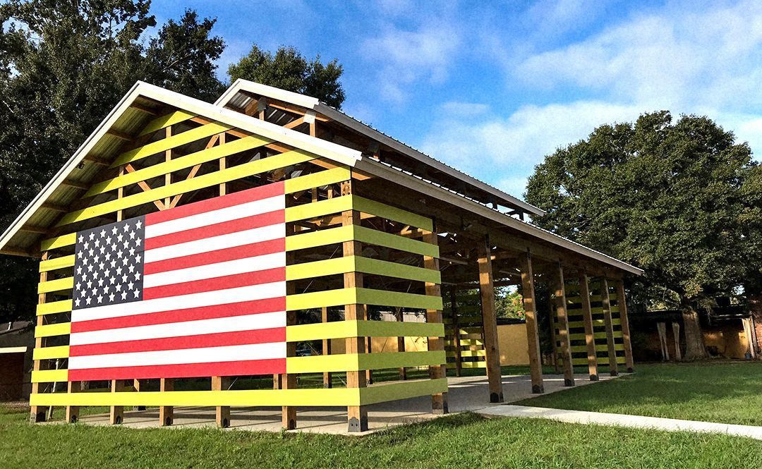 Yellow open-air structure with US flag on side, green grass, and trees under a blue sky.