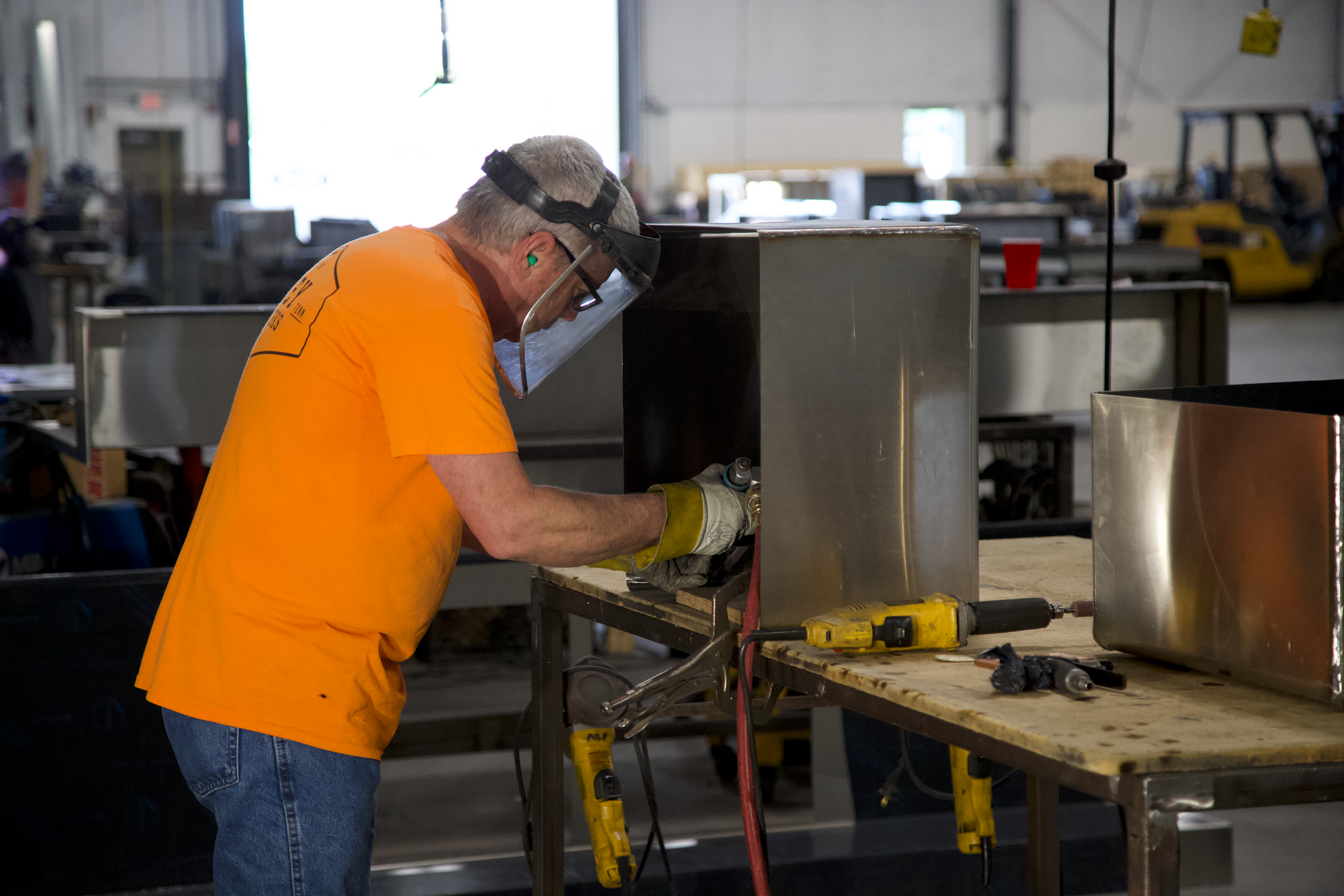 A man wearing a welding mask is working on a piece of metal in a factory.