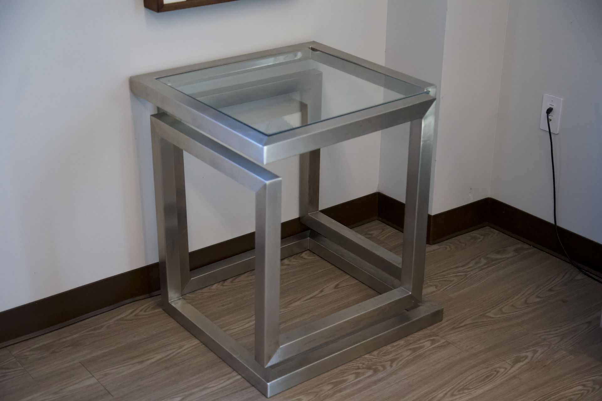 A small table with a glass top is sitting on a wooden floor in a room.