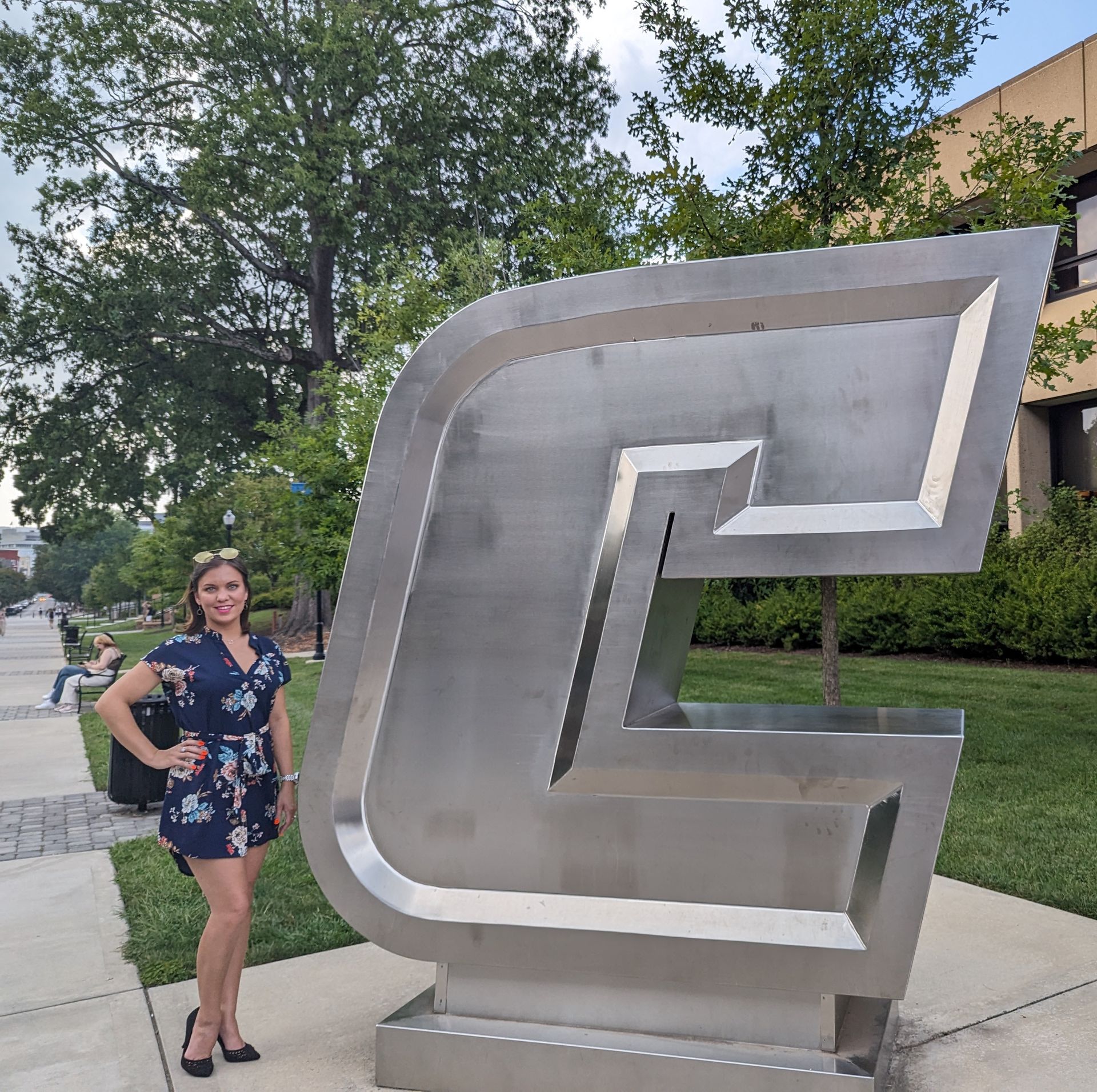 A woman stands in front of a large silver letter g
