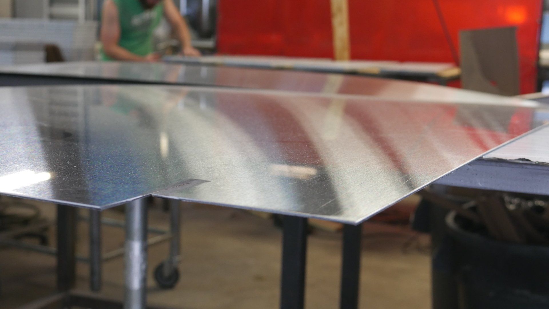 A person is standing behind a table with a piece of metal on it.