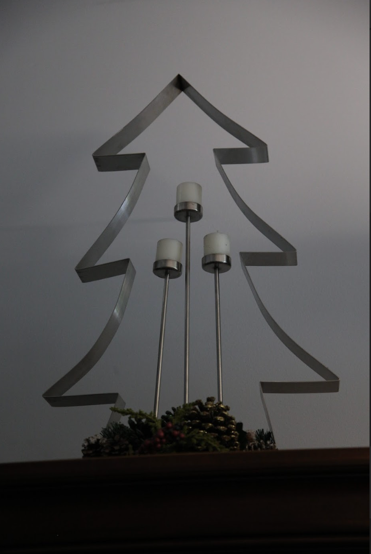 A metal christmas tree with three candles in it