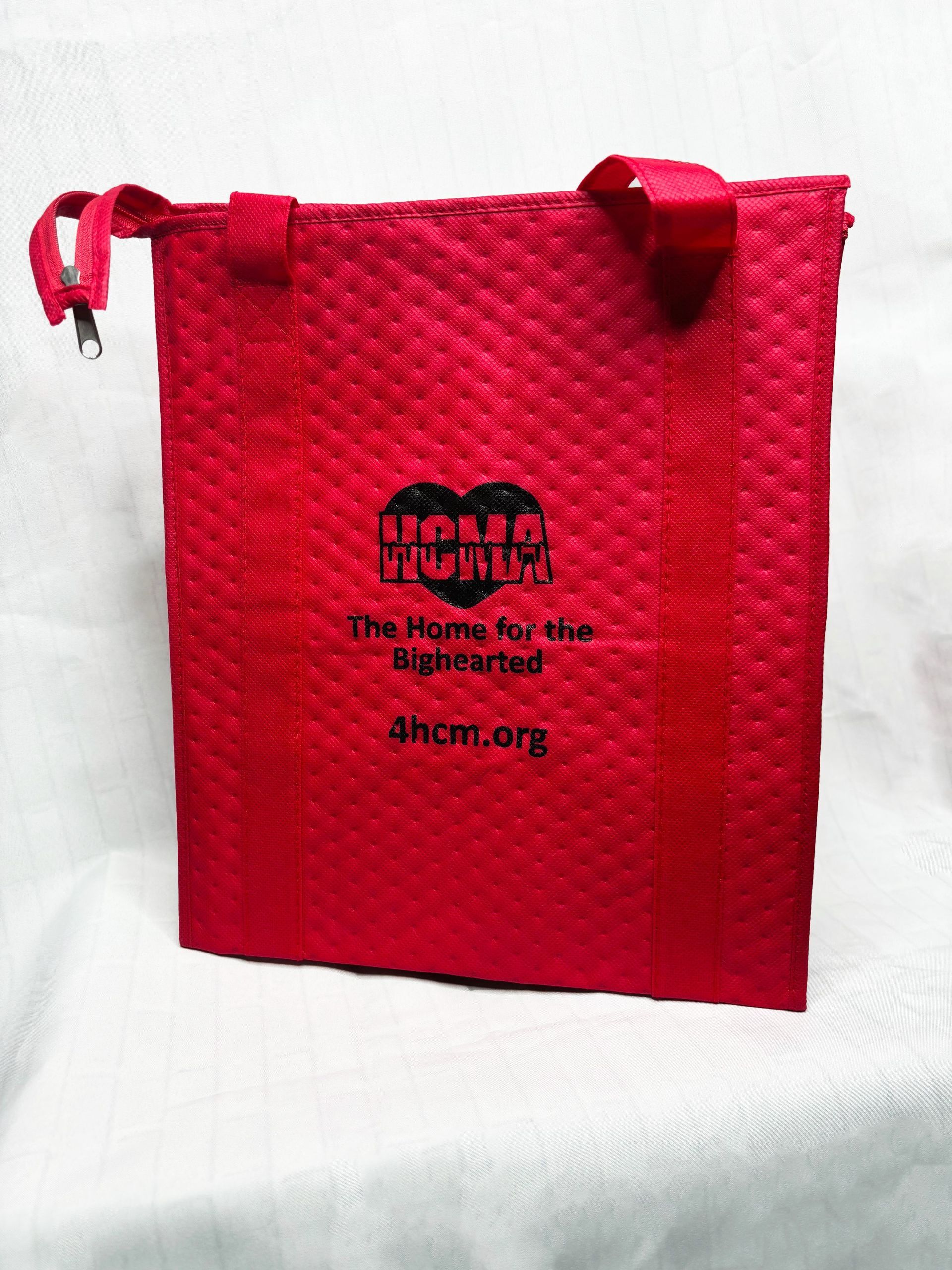 Photo of a red thermal zipper bag with a dotted indent pattern and the HCMA logo in black with text: The Home for the Bighearted