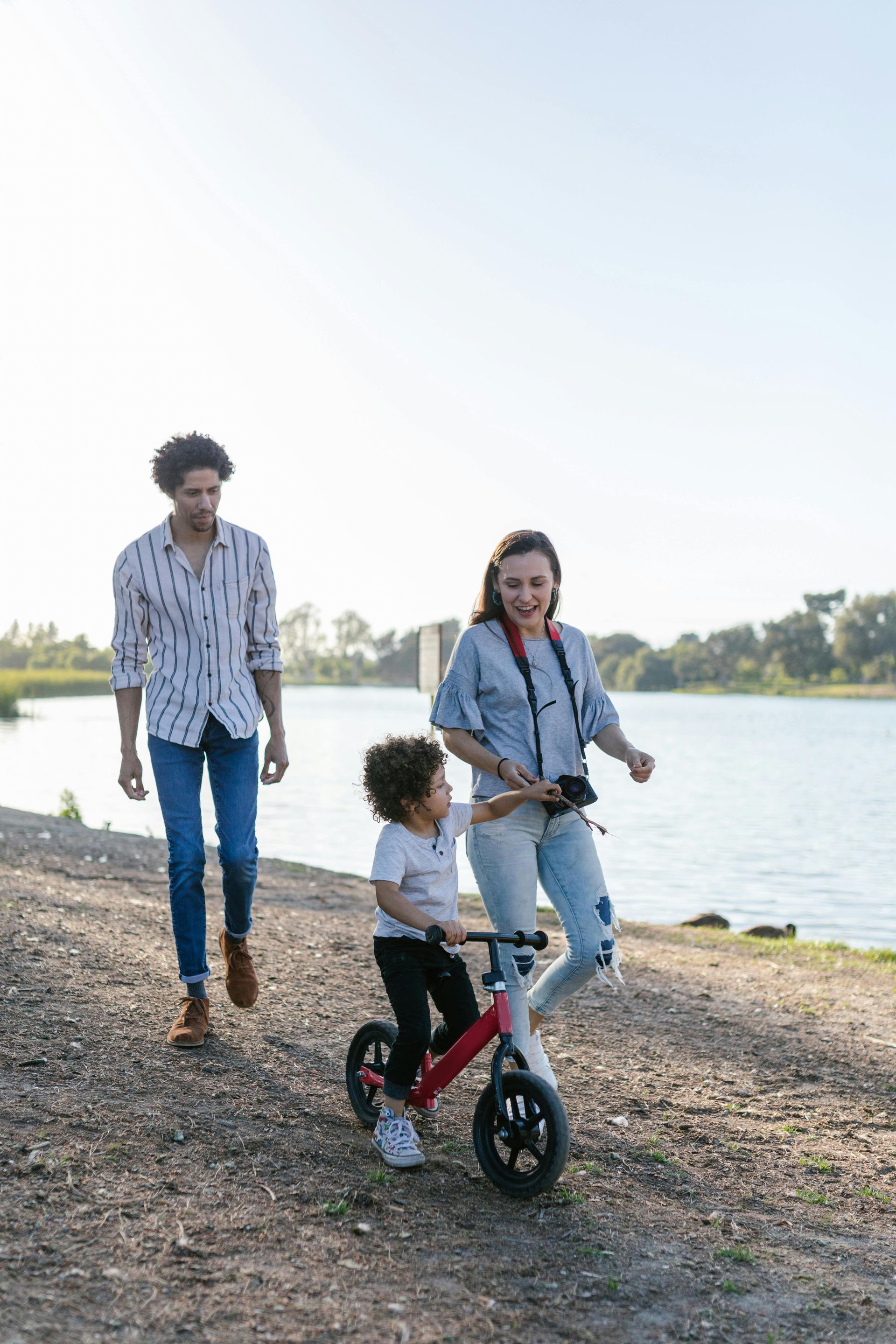 A mixed race family in denim walks down a road, the child on a tricycle