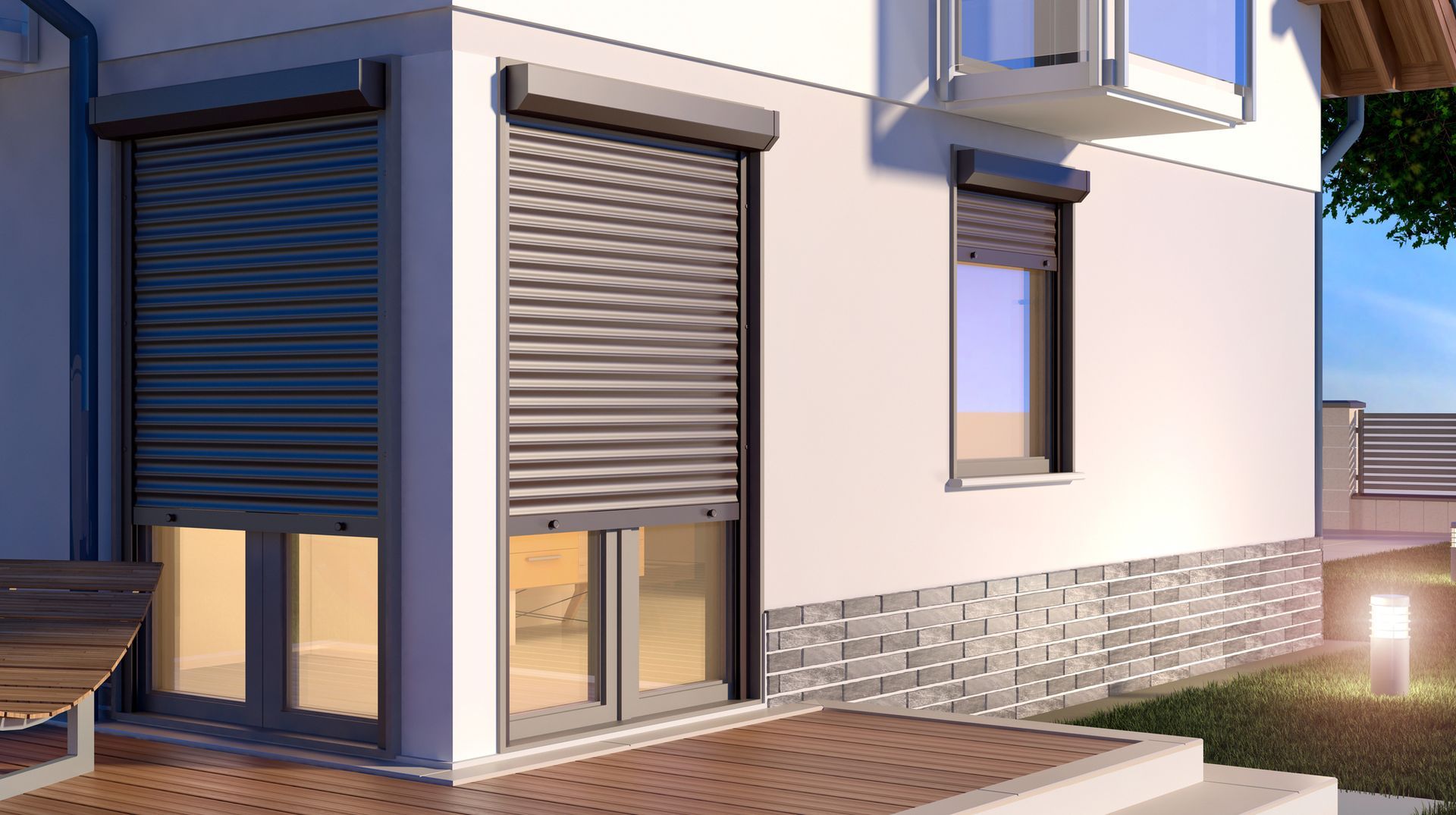Esterno di una casa moderna con tapparelle grigie, base in mattoni e un piccolo patio al tramonto.
