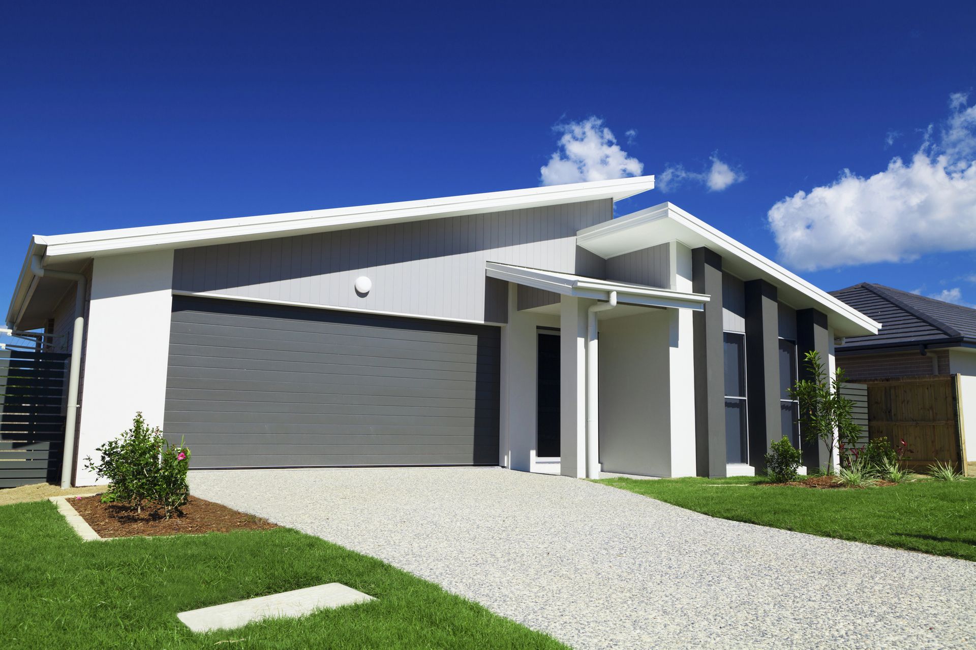 Casa moderna a un solo piano con porta del garage grigia, esterni bianchi e vialetto di ghiaia sotto un cielo azzurro
