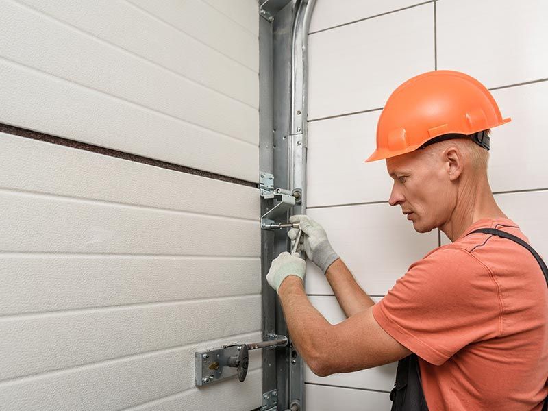 A man in an orange hard hat is engaged in garage door repair in Winnemucca, NV, reflecting dedicatio